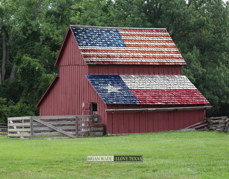 a red barn with an american flag painted on it's roof in front of trees