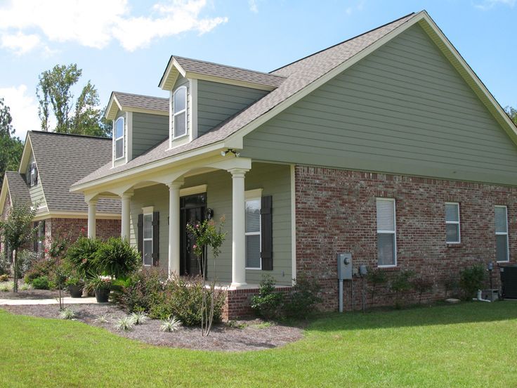 a brick house with green grass and bushes in the front yard on a sunny day