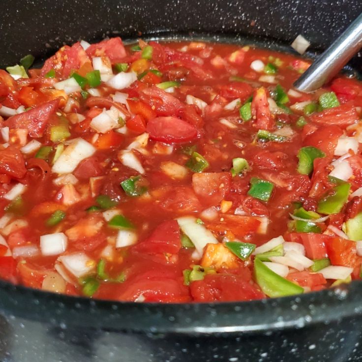 tomatoes, onions and green peppers are being cooked in a pot on the stove top