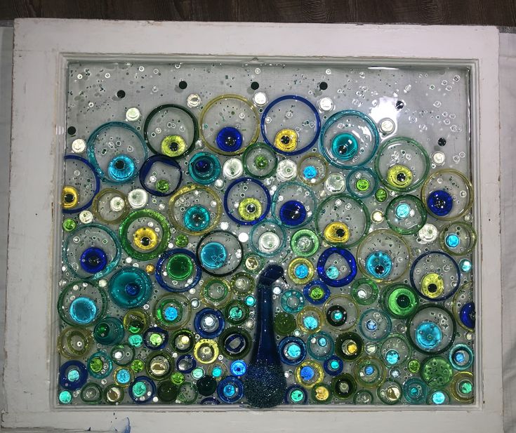 a peacock made out of glass sitting on top of a window sill in front of a wall