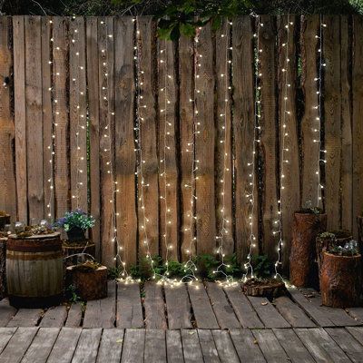 a wooden fence with lights hanging from it and potted plants on the ground next to it