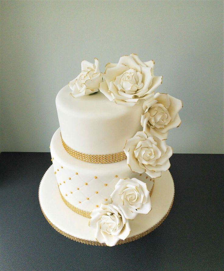 a three tiered cake with white flowers on top and gold trim around the edges