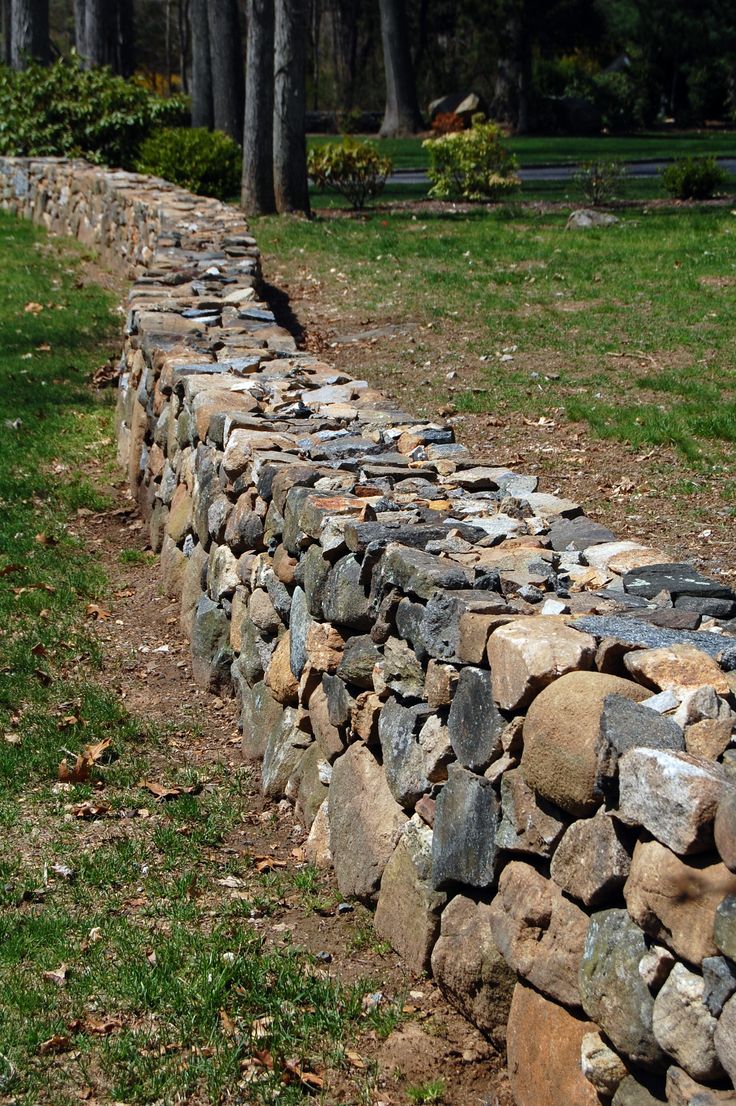 a stone wall in the middle of a grassy field