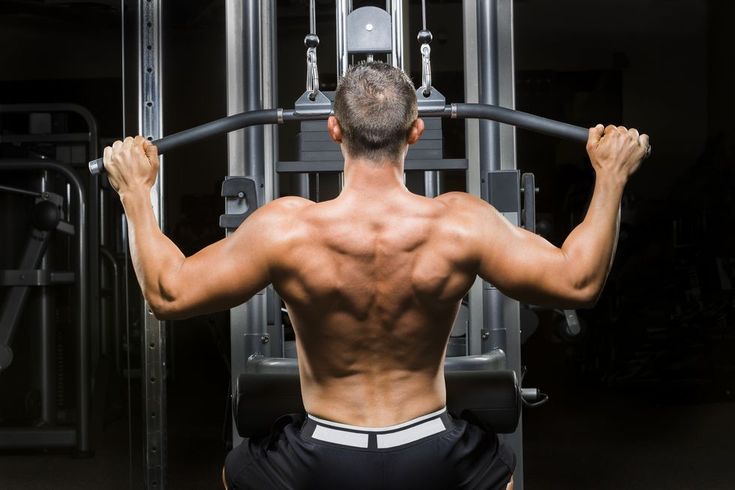 a man with no shirt on working out in a gym area at the bottom of a pull up bar