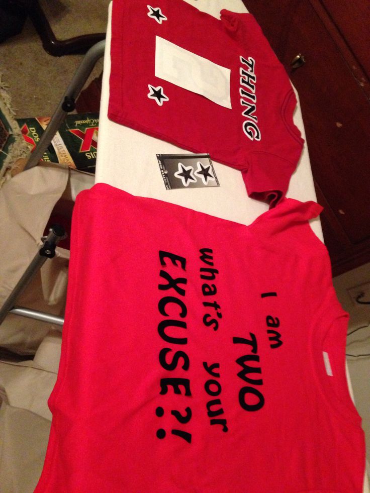 three red shirts with white and black letters on them sitting on top of a table