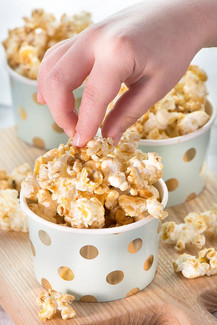 a person is picking up some popcorn out of a white bowl on a wooden board