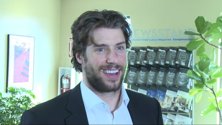 a man in a suit and white shirt is smiling at the camera while standing next to a plant