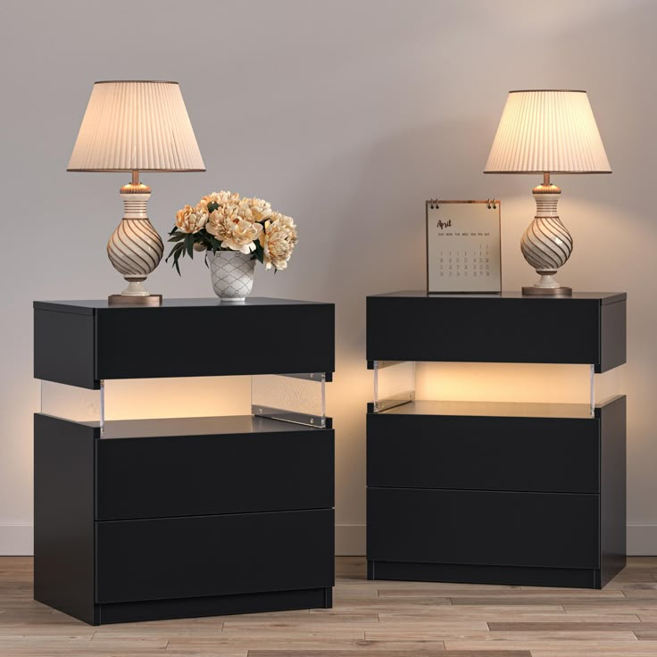 two black night stands with flowers on top and one lamp on the side next to each other