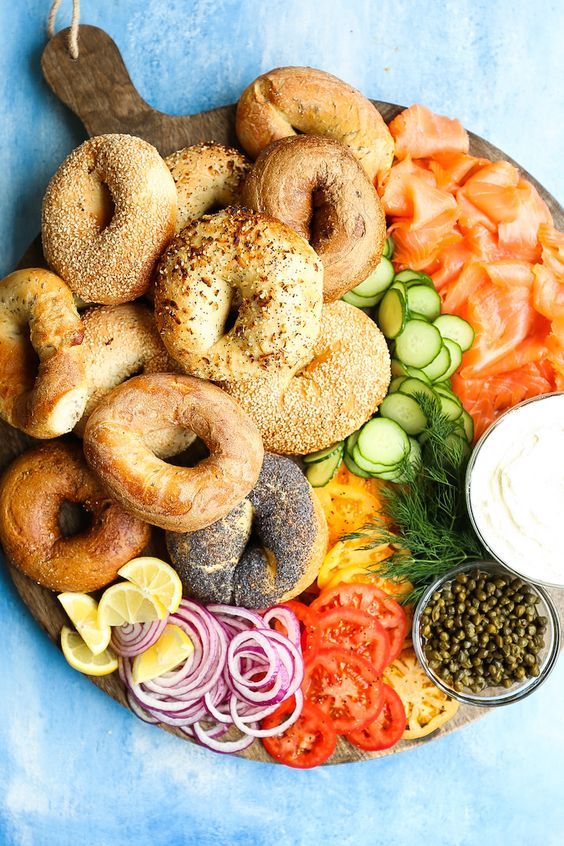 a platter with bagels, tomatoes, cucumbers, onion rings and other foods