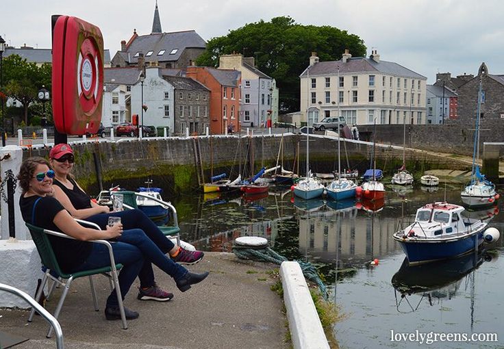 two women sitting on chairs next to the water with boats in the harbor behind them