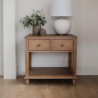 a wooden table with two drawers and a white lamp on it next to a wall