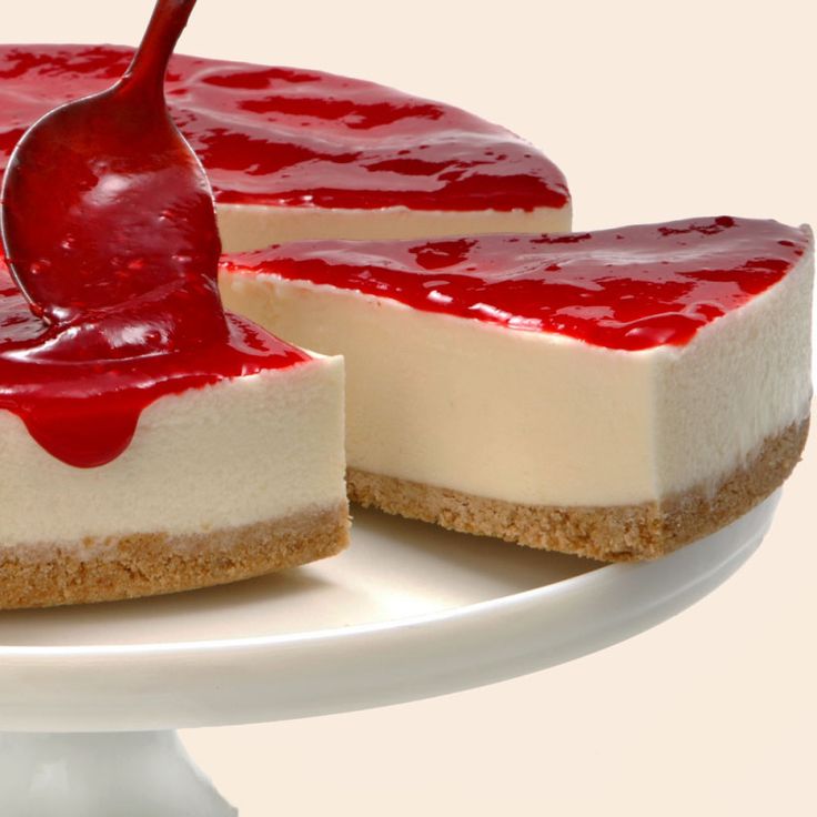 a piece of cheesecake on a white plate with a red sauce being drizzled over it