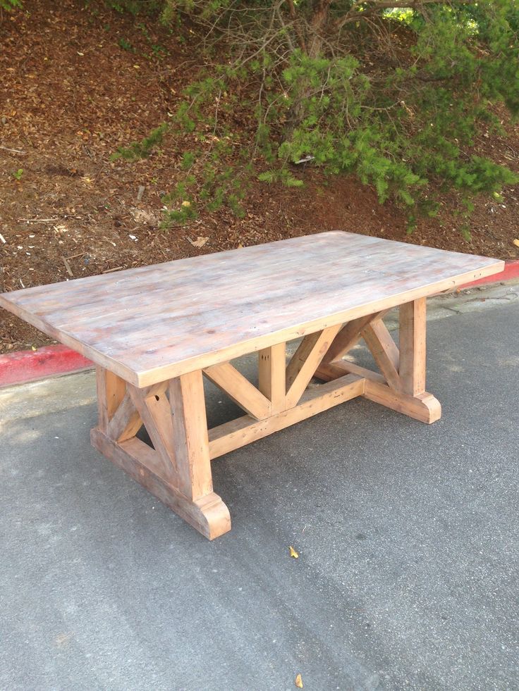 a wooden table sitting in the middle of a parking lot next to trees and bushes