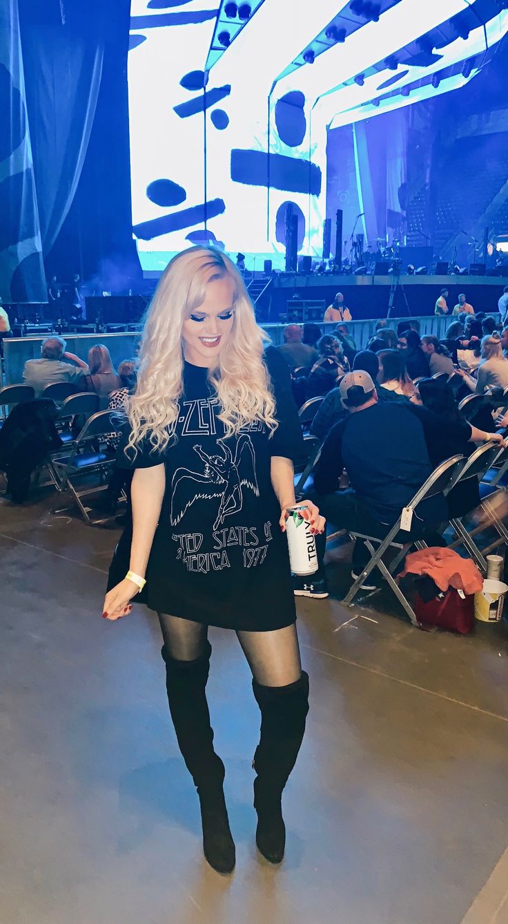 a woman with long blonde hair and black boots standing in front of a large crowd