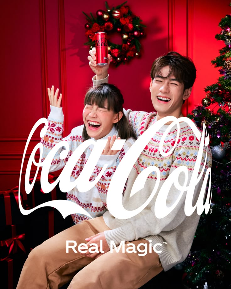 two people sitting next to each other in front of a christmas tree and coca - cola advertisement