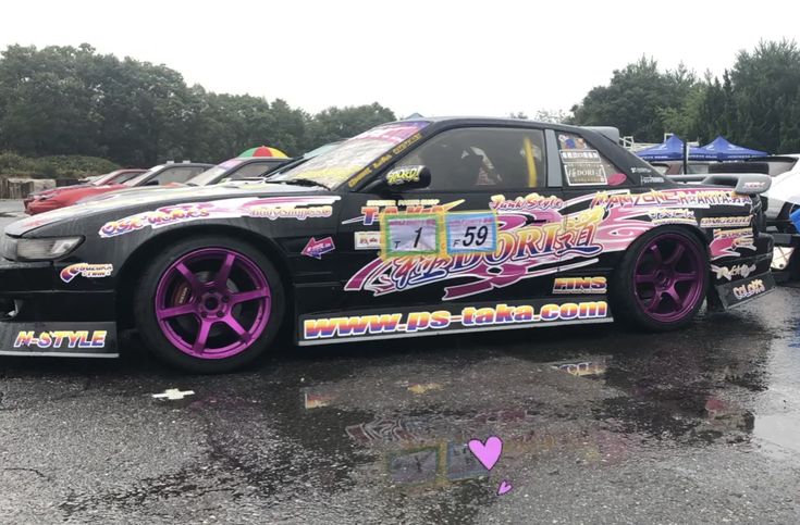 a car with pink rims parked in a parking lot next to other cars and umbrellas