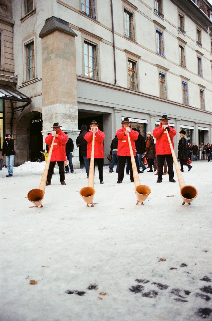 some people in red jackets are playing with baseball bats on the snow covered ground near a building