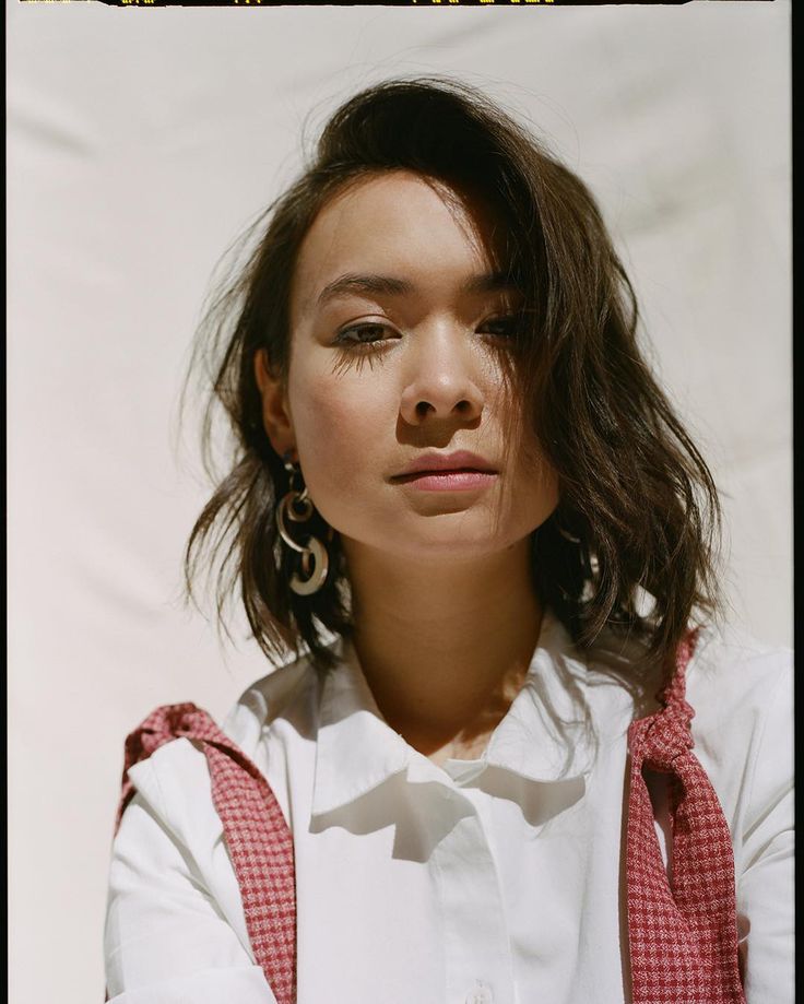 a woman with long hair wearing a white shirt and pink suspenders is looking at the camera