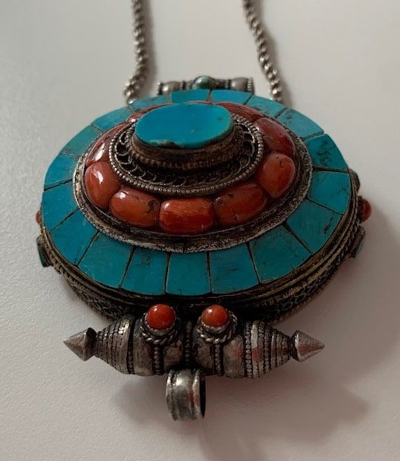 Tibetan Silver necklace with a big pendant deco with coral and turquoise ( i do not know how to open ). About prayer boxes: Traditionally, prayer boxes are used by Tibetans as portable shrines where prayers and sacred relics are kept. These prayer boxes marry that traditional concept with the Tibetan fascination for beautiful Jewelry. Tibetans write their wishes and prayers on a piece of paper and put it into the prayer box which they wear daily. By so doing, they believe that their godliness wi Traditional Turquoise Necklace With Inlay For Gift, Traditional Turquoise Inlay Necklace As Gift, Traditional Oval Handmade Necklaces, Traditional Handmade Oval Necklace, Traditional Oval Handmade Necklace, Handmade Turquoise Medallion Necklace As Gift, Handmade Turquoise Medallion Necklace Gift, Handmade Turquoise Medallion Necklace For Gifts, Traditional Turquoise Pendant Necklace