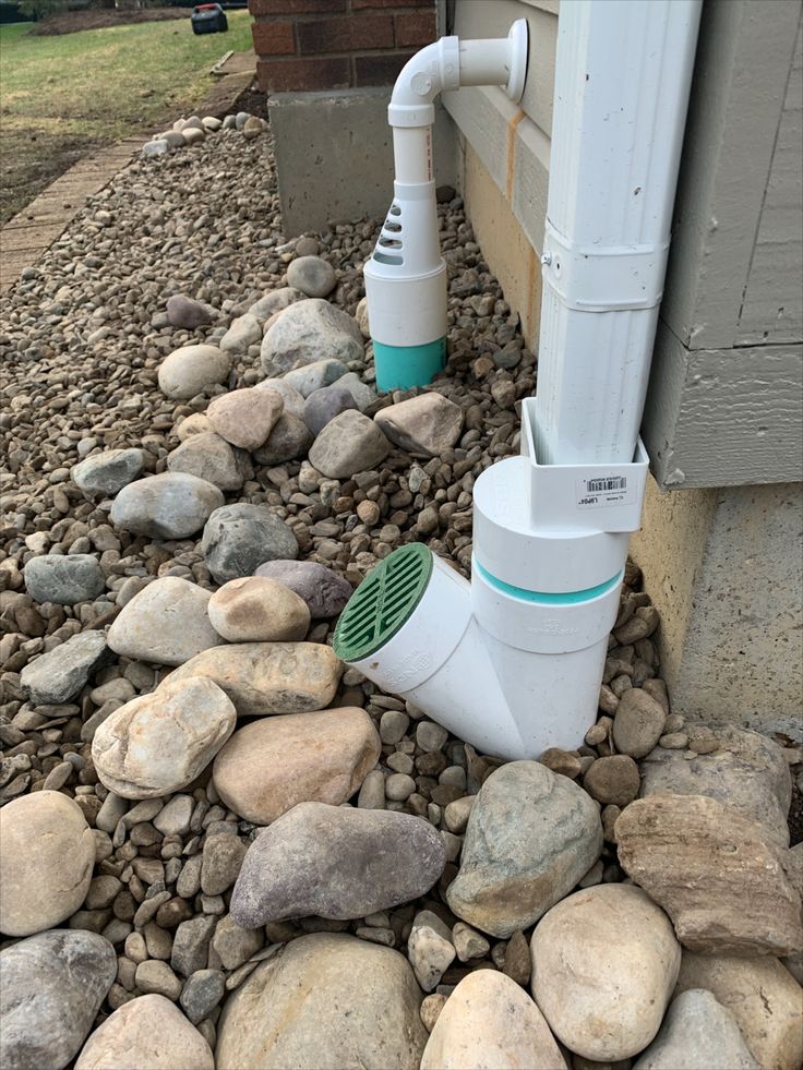 a white and green water pump sitting on top of rocks next to a house's side walk