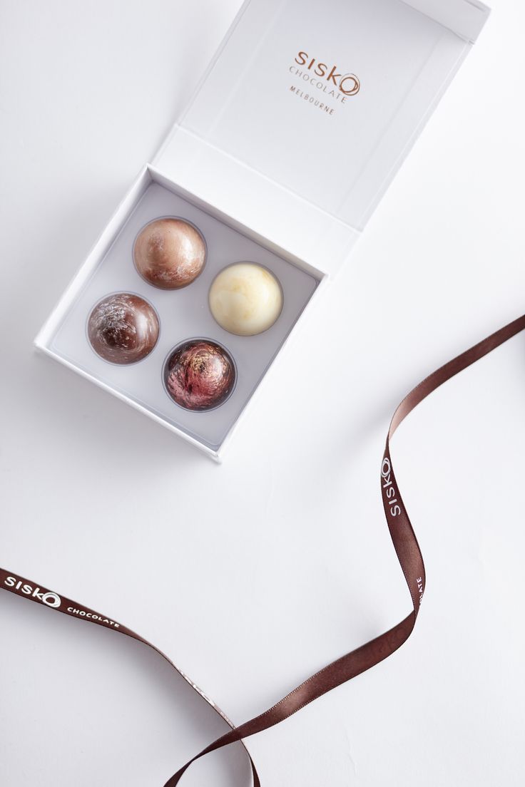 four different types of chocolates in a box with a brown ribbon on the side