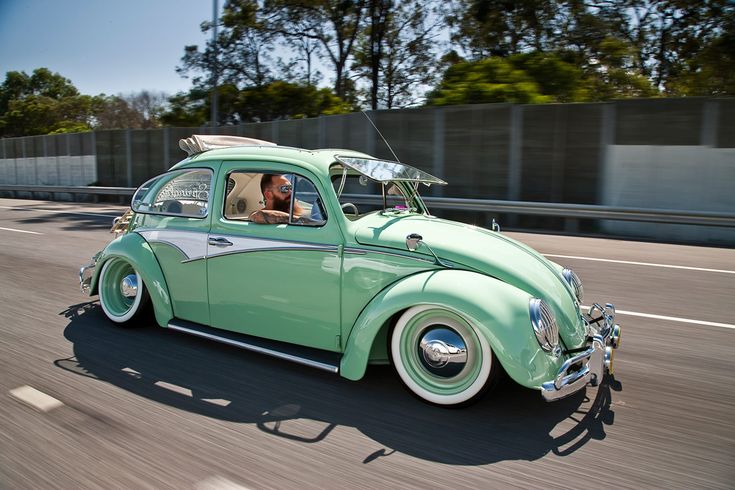 an old green car driving down the road