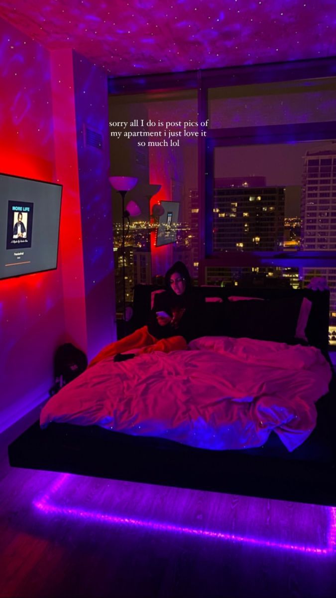 a woman sitting on a bed in a room with purple lighting and cityscape