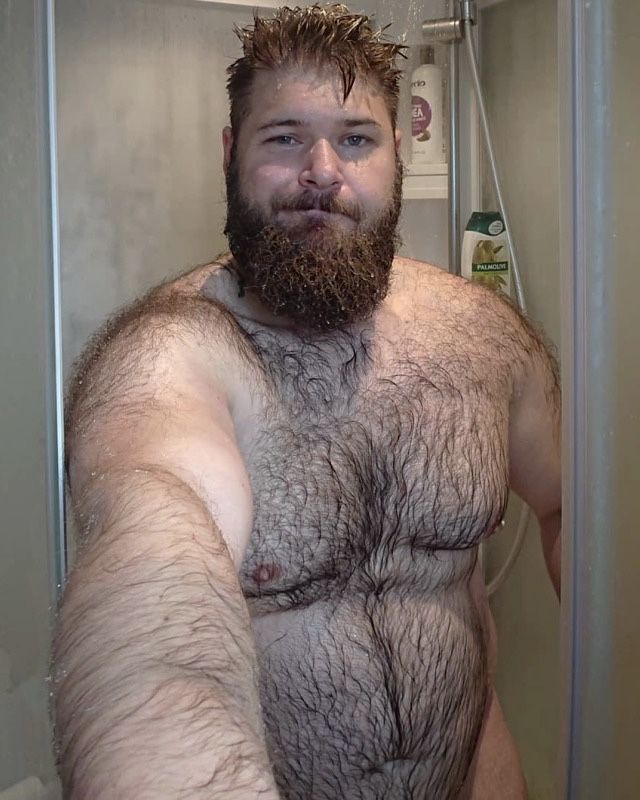 a man with a hairy beard and no shirt on in the shower holding his arms out