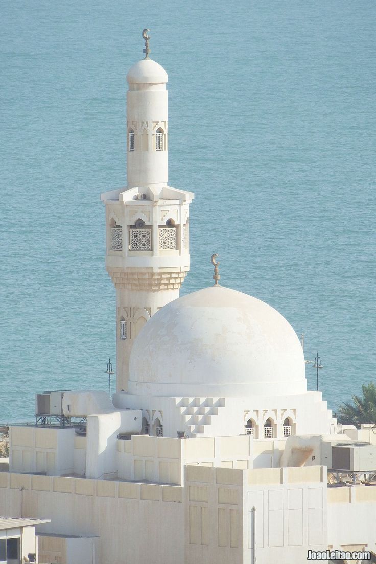 a tall white building with a clock on it's side next to the ocean