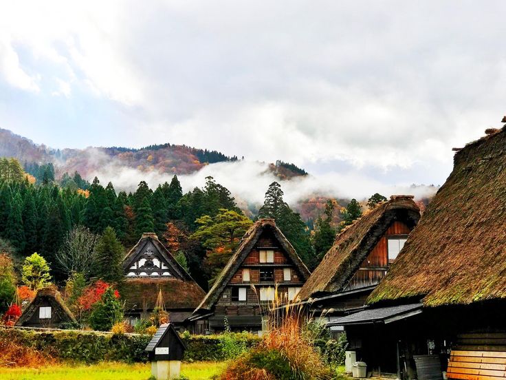 an old village with thatched roofs and trees in the backgrouds on a cloudy day