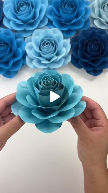 someone is holding paper flowers in front of blue and green roses on a white surface