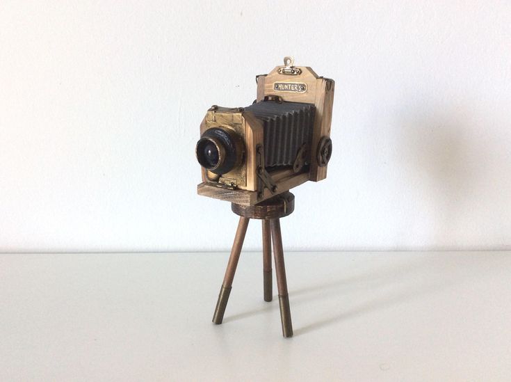 an old camera sitting on top of a wooden tripod with a white wall in the background