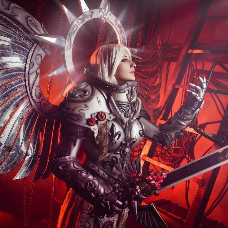 a woman dressed in armor and holding two swords with wings on her chest, standing against a red background