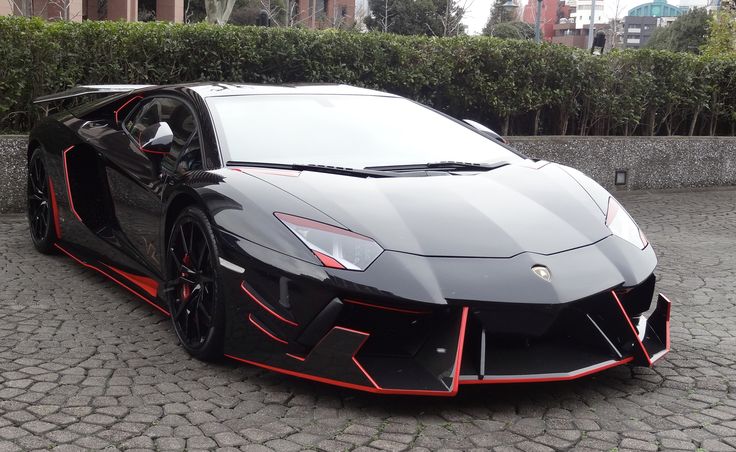 a black and red sports car parked in front of a hedged area with cobblestones