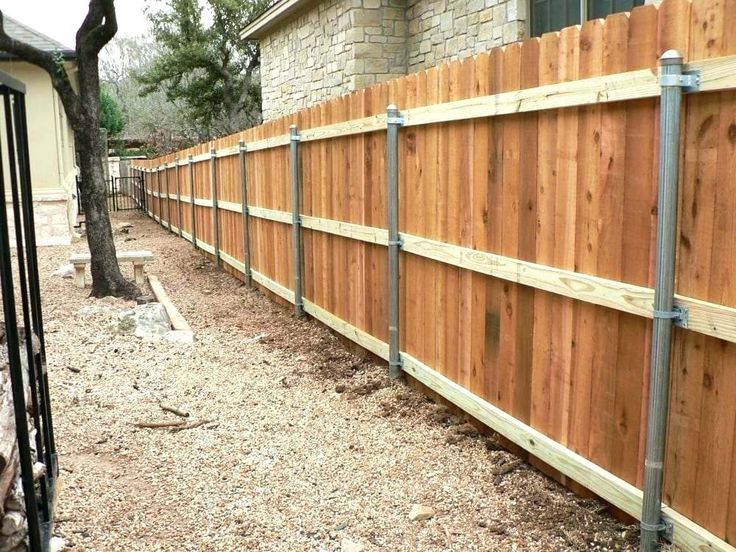 a wooden fence is next to a brick building and tree in the yard with gravel on the ground