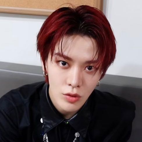 a young man with red hair wearing a black shirt and silver necklace, looking at the camera