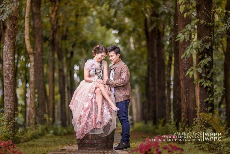 a man and woman are sitting on a statue in the middle of a path surrounded by trees