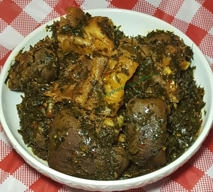 a white bowl filled with meat and greens on top of a checkered table cloth