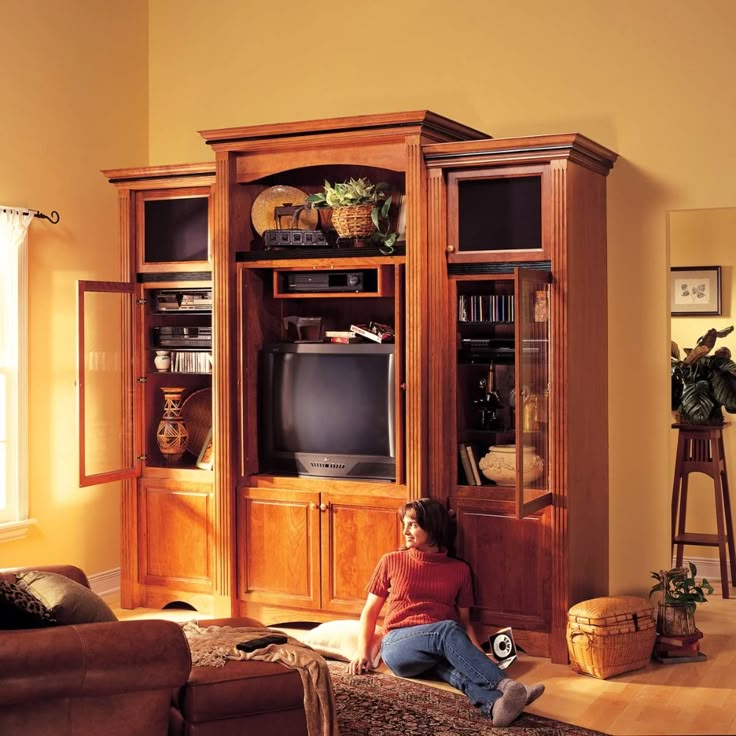 a woman sitting on the floor in front of a wooden entertainment center