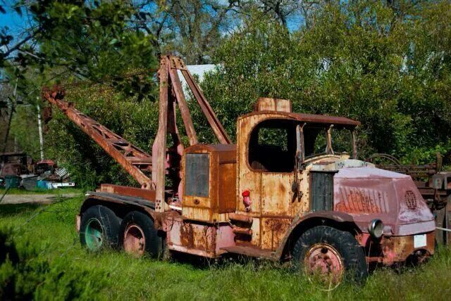 an old rusted out truck sitting in the middle of a grassy field next to trees