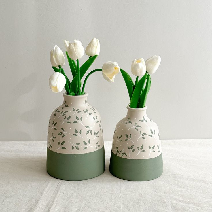 two vases with flowers in them sitting on a white tablecloth covered table cloth