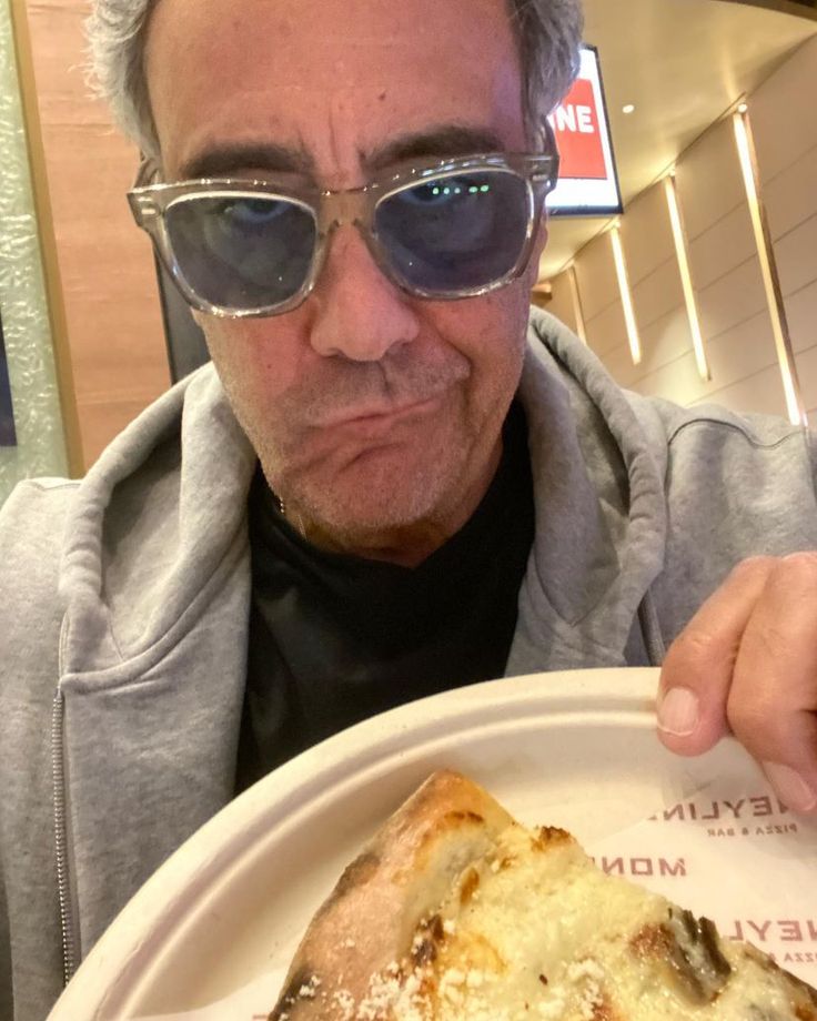 a man in sunglasses is holding up a piece of pizza on a white paper plate