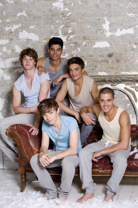 a group of young men sitting next to each other on top of a couch in front of a brick wall