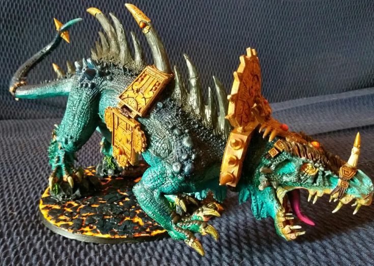 two toy dinosaurs sitting next to each other on a blue cloth covered surface with yellow and green accents