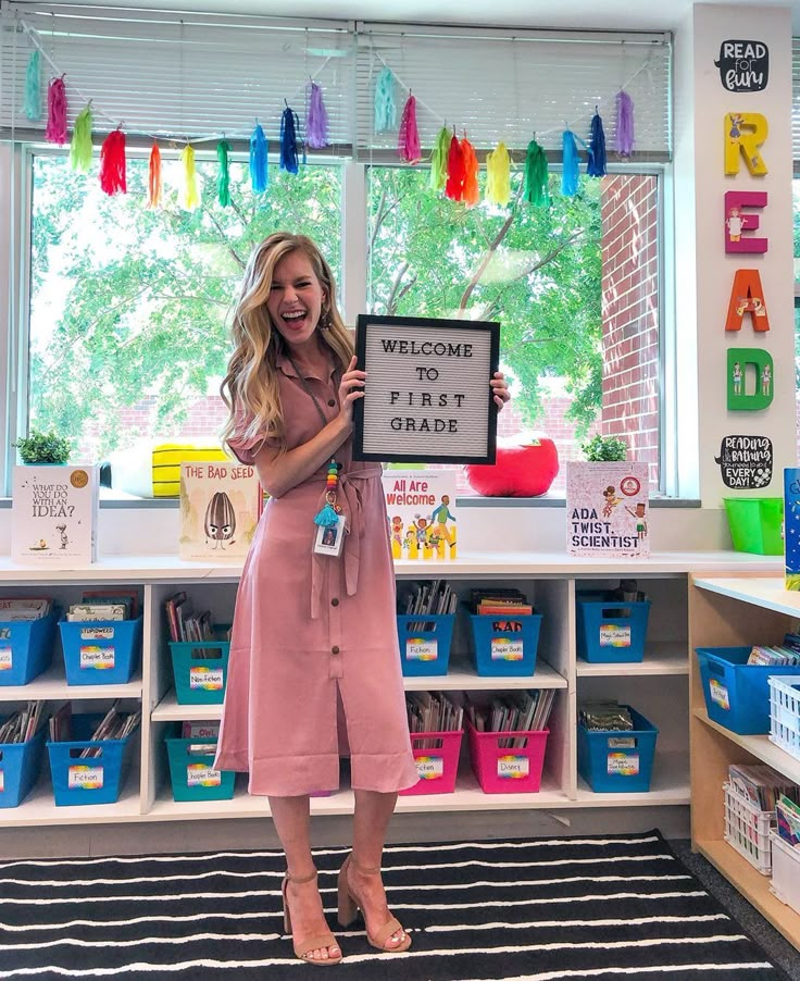 a woman standing in front of a classroom holding up a sign that says welcome first grade