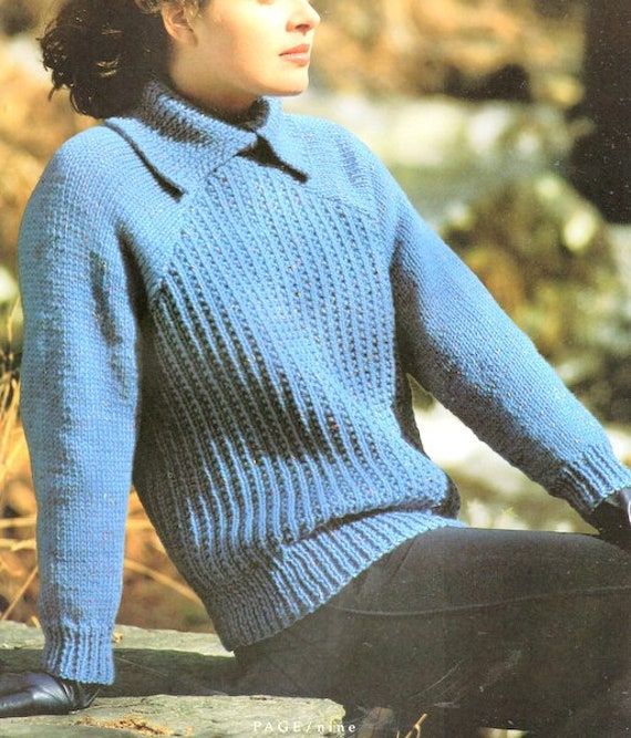 a woman sitting on top of a rock wearing a blue sweater