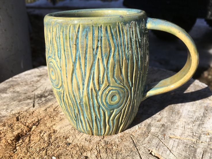 a green mug sitting on top of a tree stump in the sun with swirly designs