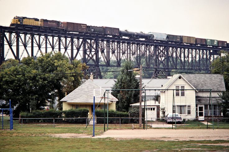 a train traveling over a bridge on top of a lush green field next to houses