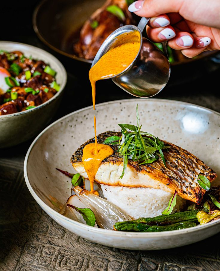 someone pouring sauce on a fish in a bowl