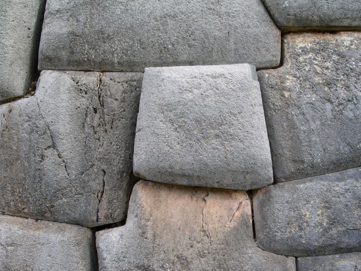 a stone wall made up of several different sized rocks and cement blocks, with small cracks in the middle